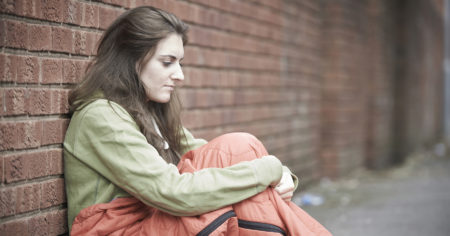 homeless girl sitting on street, victim of trafficking