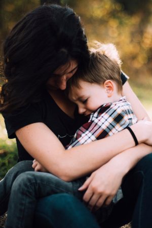 Woman sitting with boy in lap, comforting his childhood scars