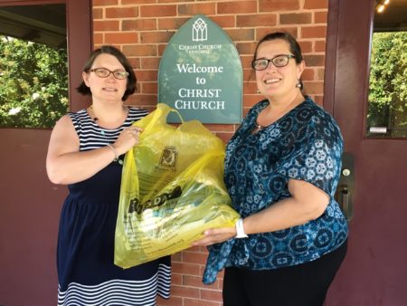 Hedrick Lewis and Debbie Rice holding filled yellow bag in front of Christ Church
